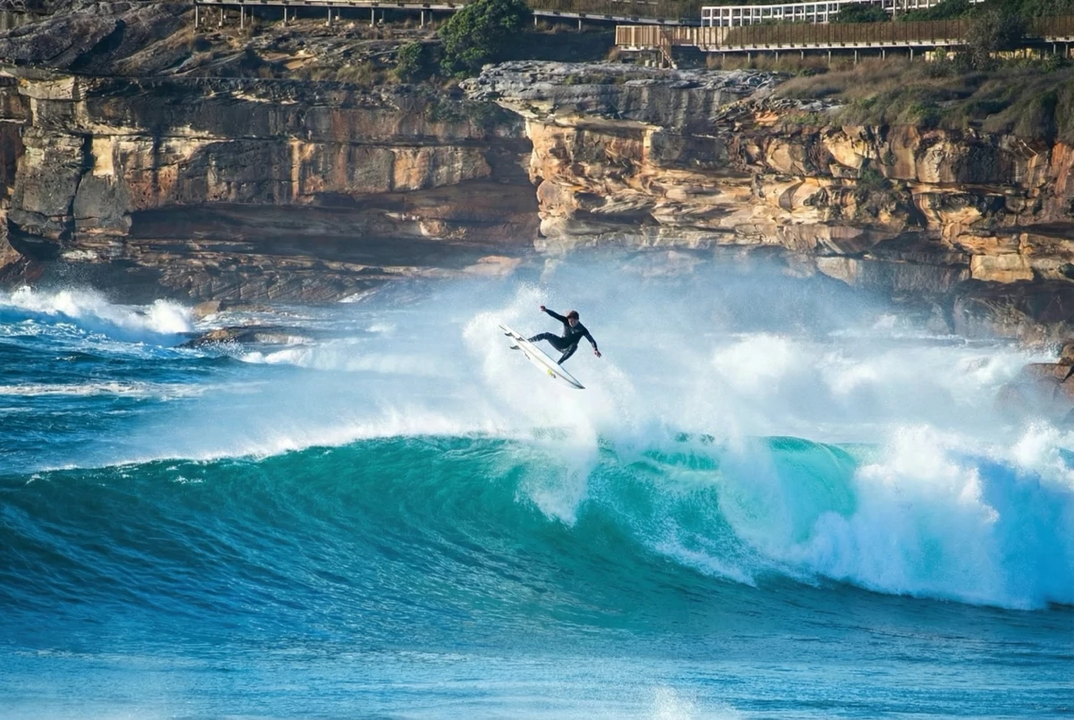 Surfer carving under a sandstone cliff
