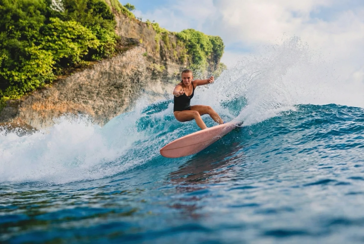 Female longboarder cutting back, tropical cliff backdrop